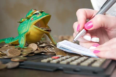 Woman's hand makes a note on the scattered coins. origin of capital and the l Stock Photos