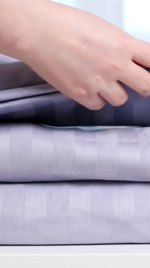Womans hand neatly folding clean, fresh striped lavender bedding, placing it on Stock Footage 343908604