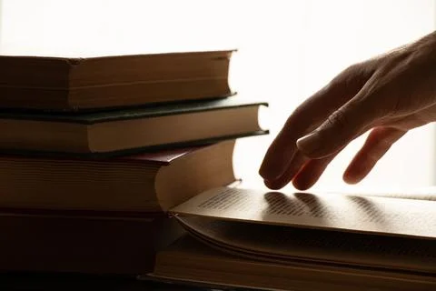 A woman's hand on an open book on a table with direct light from a window in  Stock Photos