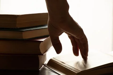 A woman's hand on an open book on a table with direct light from a window in  Stock Photos