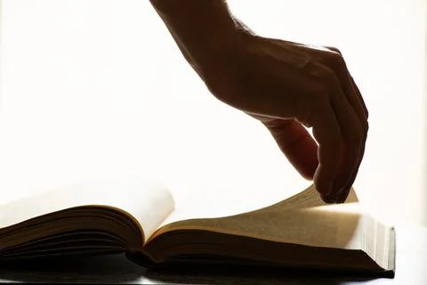 A woman's hand on an open book on a table with direct light from a window in  Stock Photos