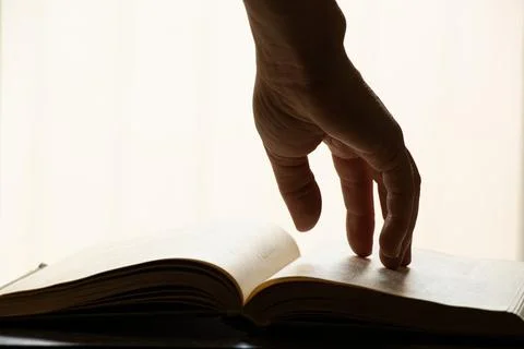 A woman's hand on an open book on a table with direct light from a window in  Stock Photos