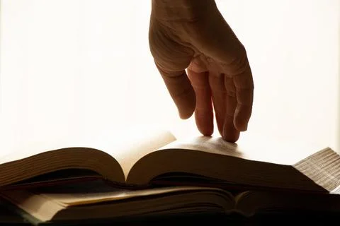 A woman's hand on an open book on a table with direct light from a window in  Stock Photos