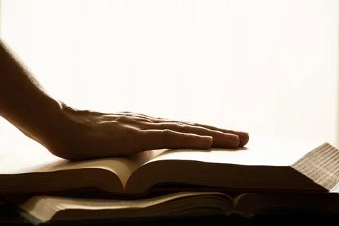 A woman's hand on an open book on a table with direct light from a window i.. Stock Photos