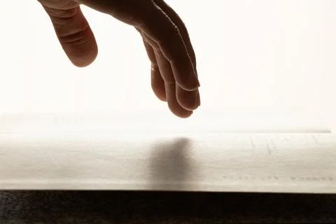 A woman's hand on an open book on a table with direct light from a window in  Stock Photos