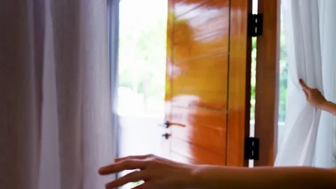 Womans hand opening white curtains to reveal bright sunny morning through g.. Stockbeeldmateriaal 333315005