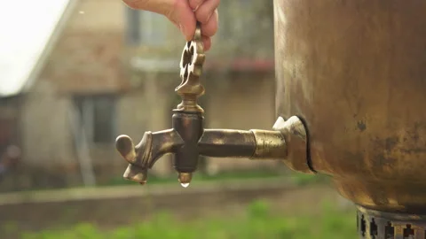 A woman's hand opens the brass tap of the samovar and boiling water flows Video stock 153936001