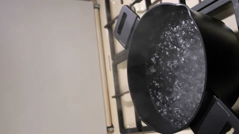 A woman's hand opens the lid of a black pot where water is boiling. Video stock 233117068