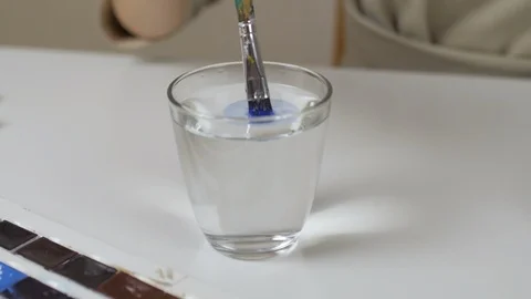 Woman's hand with a paint brush, stir in a glass of water. Work of the artist. Stock Footage 86990182