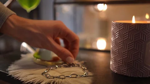 Woman's hand picking up a silver chain bracelet from a vanity table with a burni Stock Footage 328006590