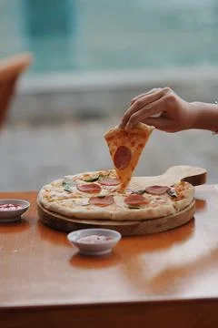 Woman's hand is picking up a slice of pizza on a blurry background Foto stock