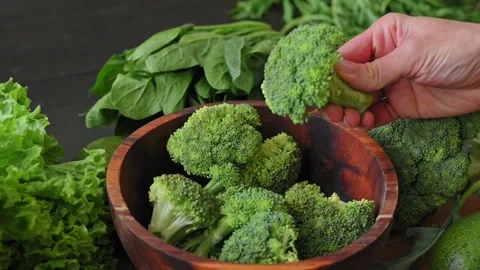 Woman's hand picks up fresh broccoli floret from wooden bowl. Healthy food Stock Footage 340026930