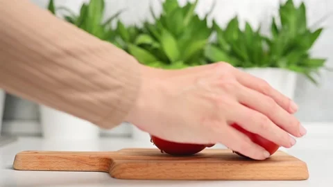 A woman's hand picks up red ripe juicy tomato from wooden cutting board on Stockbeeldmateriaal 205515448