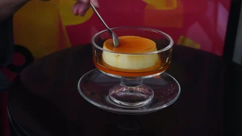 A woman's hand picks up a spoon and scoops up caramel custard pudding Vidéo 315636962