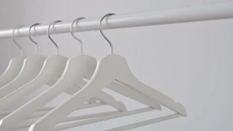 Woman's hand picks up white empty wooden hanger from rack against white wall. Stock Footage 193590476
