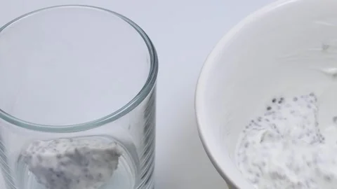 Womans hand placing thick yogurt with chia seeds into a clear glass for Stock Footage 314364079