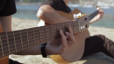 Woman's hand playing guitar on sandy beach, sunny day, close up Stock Footage 127717333