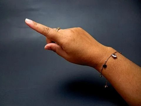 A woman's hand points forward, adorned with ring and heart charm bracelet, .. Stock Photos