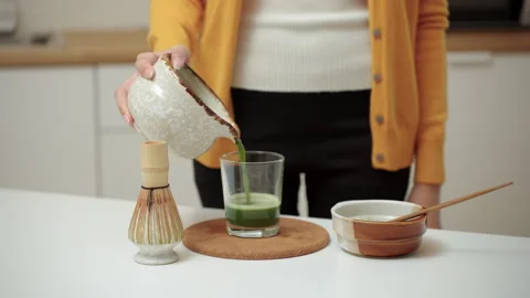 Woman's hand pouring liquid green matcha concentrate to a glass of water. Video stock 338987329