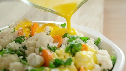 A woman's hand pours an egg mixture with over a future cauliflower casserole Stock Footage 262782042