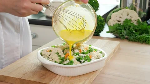 A woman's hand pours an egg mixture with over a future cauliflower casserole Stock Footage 262782044