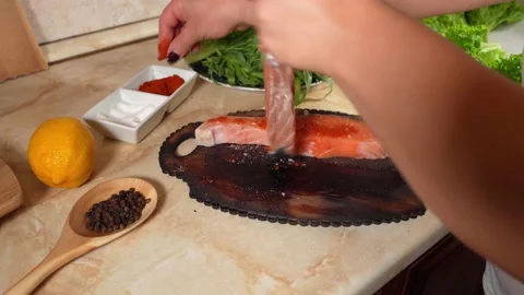 Woman's hand  pours ground red pepper  on two pieces salmon fish Stock Footage 143567743