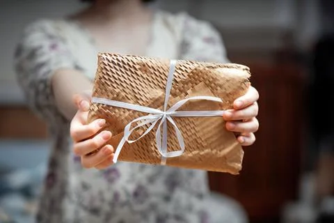 Woman's hand presents a rectangular gift wrapped in yellow netted kraft paper Foto stock