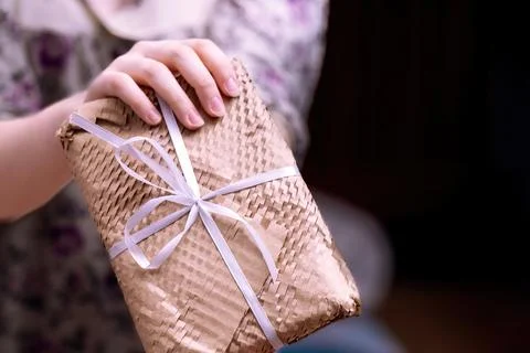 Woman's hand presents a rectangular gift wrapped in yellow netted kraft paper Stock Photos