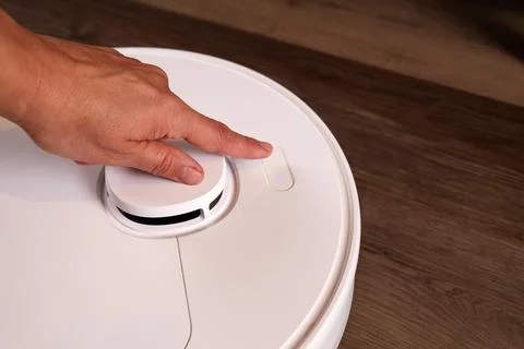 A woman's hand presses the power button of a robot vacuum cleaner Foto stock