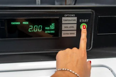 Womans hand pressing the start button on a top-loading washing machine Stock Photos