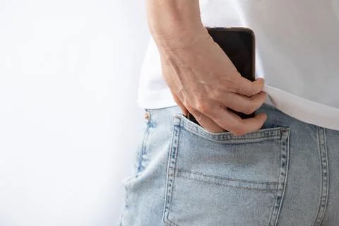 A woman's hand pulls out a mobile phone from the back pocket of her jeans. Close Stock Photos