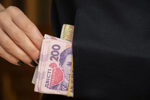 A woman's hand pulls out a pack of Ukrainian hryvnias from the pocket of a bl Stock Photos