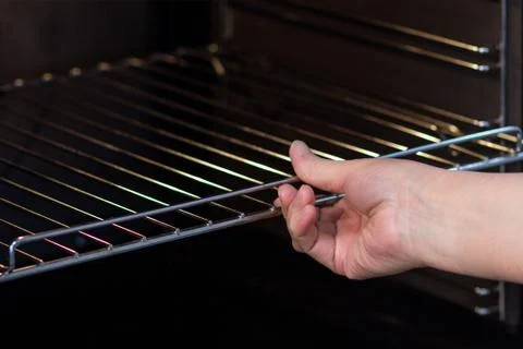 The woman's hand pushes or inserts the grate into the oven. Stock Photos