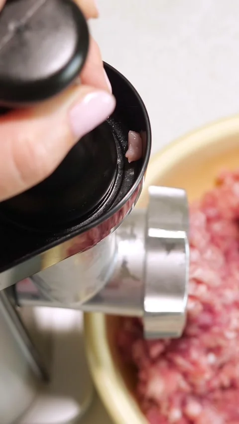 Womans hand pushing raw pork and beef with a plunger into an electric meat Stock Footage 341678659