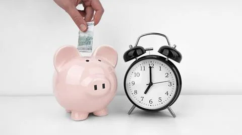 Womans hand put dollar bancnote into a piggy bank with alarm clock Stock Photos