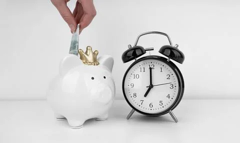 Womans hand put dollar bancnote into a piggy bank with alarm clock Stock Photos