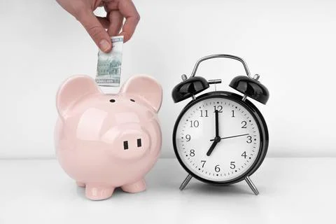 Womans hand put dollar bancnote into a piggy bank with alarm clock Stock Photos