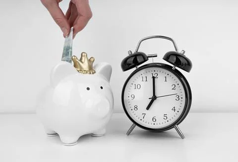 Womans hand put dollar bancnote into a piggy bank with alarm clock Stock Photos