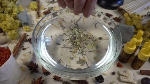 Woman's hand puts aromatic dried flowers and herbs to the glassware with a water Stock-Footage 148376460