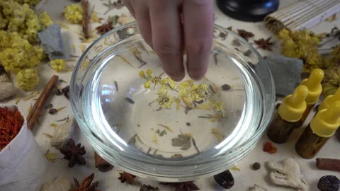 Woman's hand puts aromatic dried flowers and herbs to the glassware with a water Stock-Footage 148378191