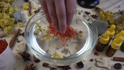 Woman's hand puts aromatic dried flowers and herbs to the glassware with a water Stock-Footage 148378341