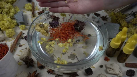 Woman's hand puts aromatic dried flowers and herbs to the glassware with a water Stock-Footage 148378432