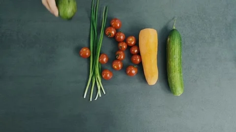 Woman's hand puts avocado on the table with one fresh cucumber, peeled carrot Stock Footage 136114063