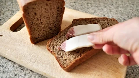 A woman's hand puts bacon on slices of black rye bread. Pieces of homemade bread Stock Footage 245070796