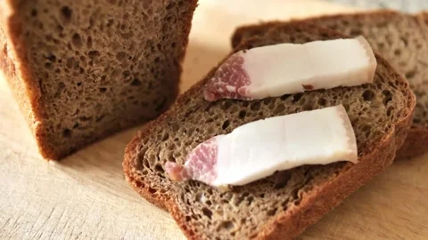 A woman's hand puts bacon on slices of black rye bread. Pieces of homemade bread Stock Footage 250325367