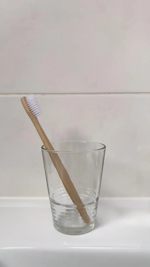 A woman's hand puts bamboo toothbrushes in a glass tumbler. 4K vertical video. Stock Footage 260695146