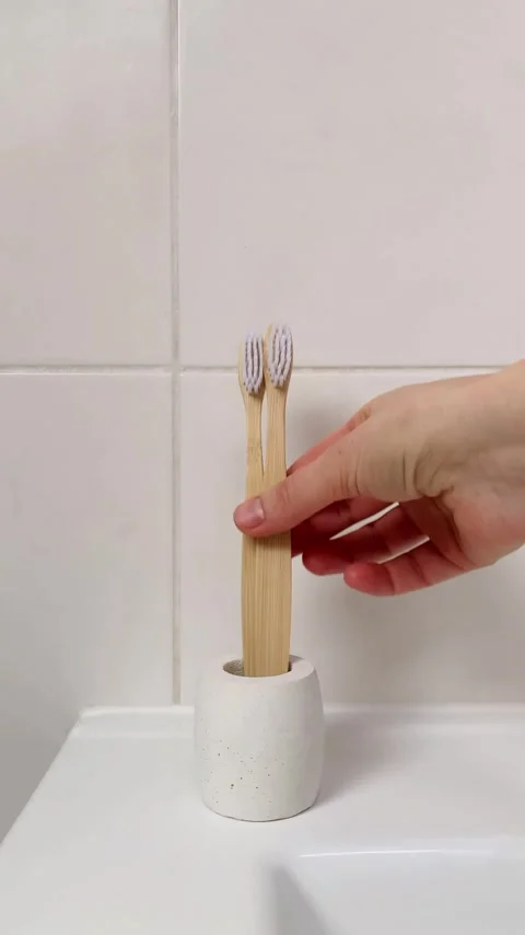 A woman's hand puts bamboo toothbrushes in a concrete stand. 4K vertical video. Stock Footage 261700764