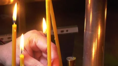 A woman's hand puts a burning candle near an orthodox cross in a church. Church Video stock 252510555