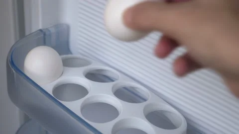 A woman's hand puts chicken eggs on a shelf in the refrigerator. The girl puts Stock-Footage 201736409