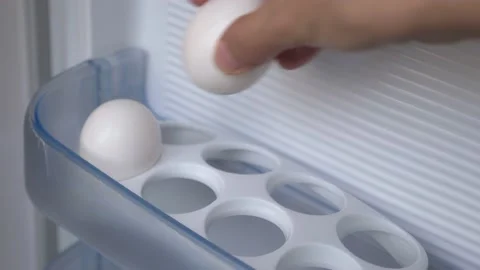 A woman's hand puts chicken eggs on a shelf in the refrigerator. Video stock 202050409